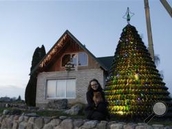 Goda Valukonyte poses by the bottle Christmas tree in the Agariniu village, Lazdijai district, some 176 kilometers (110 miles) from Vilnius, Lithuania, Saturday, Dec. 28, 2013. Lithuanian policeman Dalius Valukonis says he spent three years and hundreds of hours of his free time to create the tree using bottles he got from local restaurants, bars, family and friends. (AP Photo/Mindaugas Kulbis)
