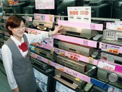 In this Oct. 31, 1998 photo, a salesclerk shows high quality VHS video casette recorders at a home and electrical appliance store in Osaka. Japanese electronics maker Funai Electric Co. says it's yanking the plug on the world's last video cassette recorder. (Kyodo News via AP)