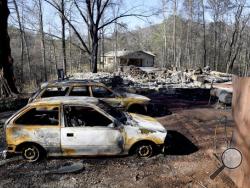 Charred home and cars sit on a property, while a neighbor's home, background, is undamaged Thursday, Dec. 1, 2016, in Gatlinburg, Tenn. A devastating wildfire destroyed numerous homes and buildings on Monday. (Michael Patrick/Knoxville News Sentinel via AP)