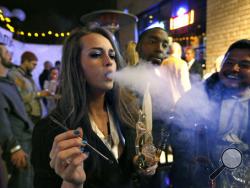 FILE - In this Dec. 31, 2013, file photo, partygoers smoke marijuana during a Prohibition-era themed New Year's Eve party at a bar in Denver, celebrating the start of retail pot sales. Denver is starting work on becoming the first city in the nation to allow marijuana clubs and public pot use in places like restaurants, yoga studios and art galleries. Voters narrowly approved the "social use" measure last November. (AP Photo/Brennan Linsley, File)