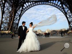 FILE - In this file photo dated Friday, Dec. 16, 2016, Rodrigo and Nancy from Mexico, pose for a photographer under the Eiffel Tower as they are on honeymoon in Paris. Paris Mayor Anne Hidalgo has pushed back at U.S. President Donald Trump for insulting the romantic city of Paris, tweeting about celebrating the attractiveness of Paris and marking the increased number of reservations from American tourists. (AP Photo/Christophe Ena, FILE)