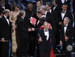 Fred Berger, producer of "La La Land," foreground center, gives his acceptance speech as members of PricewaterhouseCoopers, Brian Cullinan, holding red envelope, and Martha L. Ruiz, in red dress, and a stage manager discuss the best picture announcement error among the cast at the Oscars on Sunday, Feb. 26, 2017, at the Dolby Theatre in Los Angeles. The actual winner of best picture went to "Moonlight." (Photo by Chris Pizzello/Invision/AP)