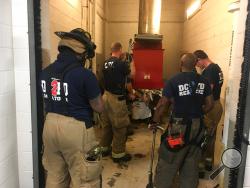 In this photo provided by DC Fire and EMS, emergency personnel respond to a call from a man who was stuck in a trash chute, early Sunday, July 23, 2017, in Washington. Spokesman Vito Maggiolo says the man was throwing out trash at the apartment building when he thought he dropped a cellphone in the chute. Maggiolo says the man leaned in to check and fell inside. (Vito Maggiolo/DC Fire and EMS Department via AP)