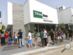 People wait in line to withdraw cash at a bank in the aftermath of Hurricane Maria, in San Juan, Puerto Rico, Wednesday, Sept. 27, 2017. A week since the passing of Maria many are still waiting for help from anyone from the federal or Puerto Rican government. But the scope of the devastation is so broad, and the relief effort so concentrated in San Juan, that many people from outside the capital say they have received little to no help. (AP Photo/Gerald Herbert)