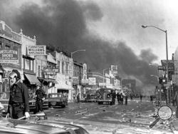 In this July 24, 1967, file photo, police check buildings along a section of 12th Street, about three miles from downtown Detroit, following racial riots which broke out in the city. Many businesses and homes were burned and looted. Former U.S. Sen. Fred Harris, the last surviving member of the Kerner Commission, says he remains haunted that the panel's recommendations on U.S. race relations and poverty were never adopted, but he is hopeful they will be one day. (AP Photo/File)