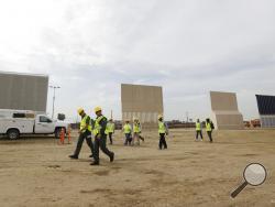 People pass border wall prototypes as they stand near the border with Tijuana, Mexico, Thursday, Oct. 19, 2017, in San Diego. Companies are nearing an Oct. 26 deadline to finish building eight prototypes of President Donald Trump's proposed border wall with Mexico. (AP Photo/Gregory Bull)