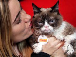 FILE - In this Nov. 14, 2016, file photo, Grumpy Cat poses for photos with her owner, Tabatha Bundesen, in New York. According to documents obtained by The Washington Post, Bundesen won a lawsuit first filed three years ago against the Grenade beverage company. She signed on for the cat to endorse a “Grumpy Cat Grumpuccino,” but the company subsequently used the cat’s image to help sell other products, which an eight-person jury on Monday, Jan. 22, 2018, found was unauthorized. (AP Photo/Richard Drew, File)
