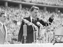 FILE - In this June 27, 1954 file photo, Evangelist Billy Graham speaks to over 100,000 Berliners at the Olympic Stadium in Berlin, Germany. Graham, who died Wednesday, Feb. 21, 2018, at his home in North Carolina's mountains at age 99, reached hundreds of millions of listeners around the world with his rallies and his pioneering use of television. Graham's body will be brought to his hometown of Charlotte on Saturday, Feb. 24, as part of a procession expected to draw crowds of well-wishers. (AP Photo/Werne