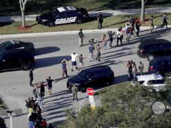 FILE - In this Feb. 14, 2018 file photo, students hold their hands in the air as they are evacuated by police from Marjory Stoneman Douglas High School in Parkland, Fla., after a shooter opened fire on the campus. Emergency calls from parents and students during the Florida high school massacre show 911 operators at first trying to grasp the enormity of the emergency and then calmly trying to gather information to assist arriving law enforcement officers. The officers arrive to find chaos as delays allowed 