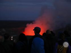 Visitors take pictures as Kilauea's summit crater glows red in Volcanoes National Park, Hawaii, Wednesday, May 9, 2018. Geologists warned Wednesday that Hawaii's Kilauea volcano could erupt explosively and send boulders, rocks and ash into the air around its summit in the coming weeks. (AP Photo/Jae C. Hong)