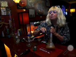 FILE - In this April, 12, 2017 file photo, Linda Wood smokes a concentrated form of marijuana called a "dab" at the Speakeasy Vape Lounge, one of the United States' only legal pot clubs, in Colorado Springs, Colo. Industry advocates say Gov. John Hickenlooper's June 4, 2018 veto of a bill allowing tasting rooms inside marijuana retailers will ensure that clubs like Speakeasy continue to operate without state regulation. (AP Photo/Thomas Peipert, File)