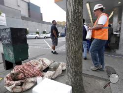 In this May 24, 2018, photo, a man sleeps on the sidewalk as people behind line-up to buy lunch at a Dick's Drive-In restaurant in Seattle. Seattle city leaders say they'll work to repeal the tax passed just last month on businesses such as Amazon and Starbucks designed to help pay for homeless services and affordable housing. Amazon and other businesses had sharply criticized the levy, and the online retail giant even temporarily halted construction planning on a new high-rise building near its Seattle hea