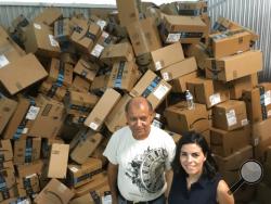 In this photograph taken June 24, 2018, Catholic Charities of the Rio Grande Valley staffer Eli Fernandez and volunteer Natalie Montelongo pose for a photo as they stand by a pile of unsorted Amazon boxes packed with donations in McAllen, Texas. A rest center for asylum-seekers in the Texas border town of McAllen has seen such a big surge of donations that they've had to rent additional storage space, and caravans of volunteers from across the U.S. have also showed up at their doors. (AP Photo/Manuel Valdes