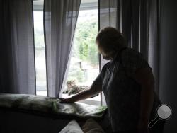  In this Wednesday, June 27, 2018 photo, Darin Martin, 58, looks at one of her cats napping on her living room window of her home in Penn Hills, Pa. Martin cared for her husband, Steve Martin, in his final days, when he told her he saw a vision of their deceased dog, Czar, walking down the hallway" (Stephanie Strasburg/Pittsburgh Post-Gazette via AP)