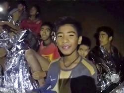 In this July 3, 2018, image taken from video provided by the Royal Thai Navy Facebook Page, Thai boys smile as Thai Navy SEAL medic help injured children inside a cave in Mae Sai, northern Thailand. The Thai soccer teammates stranded more than a week in the partly flooded cave said they were healthy on a video released Wednesday, as heavy rains forecast for later this week could complicate plans to safely extract them. (Royal Thai Navy Facebook Page via AP)