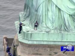 In this image made from video by PIX11, a person, center, leans against the robes of the Statue of Liberty on Liberty Island, as one of the police officers climbed up on a ladder to stand on a ledge nearby talking the climber into descending in New York, Wednesday, July 4, 2018. (PIX11 via AP)