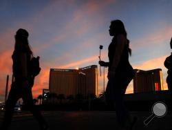 FILE - In this April 1, 2018 file photo, people carry flowers as they walk near the Mandalay Bay hotel and casino during a vigil for victims and survivors of a mass shooting in Las Vegas. MGM Resorts International has sued hundreds of victims of the deadliest mass shooting in modern U.S. history in a bid to avoid liability for the gunfire that rained down from its Mandalay Bay casino-resort in Las Vegas. The company argues in lawsuits filed Friday, July 13, 2018, in Nevada and California that it has "no lia