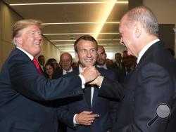 In this July 11, 2018, photo, U.S. President Donald Trump, left, shakes hands with Turkey's President Recep Tayyip Erdogan, right, as French President Emmanuel Macron, center, watches on the sidelines of a summit of heads of state and government at NATO headquarters in Brussels Belgium. Plenty of U.S. presidents have created commotion in their travels abroad, none so much as President Donald Trump. Historians say Trump’s tumultuous trip across Europe smashed the conventions of American leaders on the world 