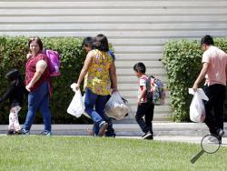 Children arrive with adults and Lutheran Social Services workers at Lutheran Social Services, Thursday, July 26, 2018, in Phoenix. Lutheran Social Services said they were expecting 75-100 reunited families separated at the border when apprehended entering the United States to come through their facility. (AP Photo/Matt York)