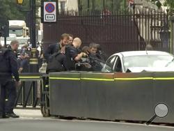 In this frame grab taken Tuesday, Aug. 14, 2018 armed police train their weapons on a car crashed into security barriers outside the Houses of Parliament stands to the right of a bus in London. London police say that a car has crashed into barriers outside the Houses of Parliament and that there are a number of injured. (ITN via AP)
