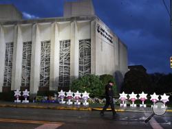 A Pittsburgh Police officer walks past the Tree of Life Synagogue and a memorial of flowers and stars in Pittsburgh on Sunday, Oct. 28, 2018, in remembrance of those killed and injured when a shooter opened fire during services Saturday at the synagogue. (AP Photo/Gene J. Puskar)