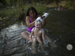 Honduran migrant Madeline Rivera, 25, washes the hair of her daughter Dariana, 5, in the Novillero River in Tapanatepec, Mexico, Sunday, Oct. 28, 2018. Thousands of migrants who are part of a caravan of Central Americans trying to reach the U.S. border took a break Sunday in Tapanatepec, on their long journey toward the U.S. border. (AP Photo/Rodrigo Abd)