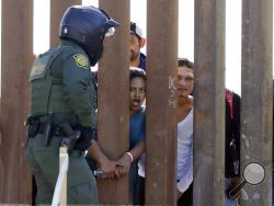 Migrants from Central America yell through a border wall at a U.S. Border Patrol agent after he pulled down a banner Sunday, Nov. 25, 2018, in San Diego. Migrants approaching the U.S. border from Mexico were enveloped with tear gas Sunday after a few tried to breach the fence separating the two countries. (AP Photo/Gregory Bull)