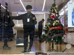In this Saturday, Dec. 22, 2018, photo, a sales person waits for customers near a Christmas tree decoration in Zhangjiakou in northern China's Hebei province. At least four Chinese cities and one county have ordered restrictions on Christmas celebrations this year. Churches in another city have been warned to keep minors away from Christmas, and at least ten schools nationwide have curtailed Christmas on campus, The Associated Press has found. (AP Photo/Ng Han Guan)
