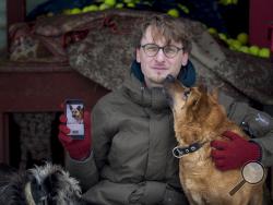 In this photo taken on Saturday, Feb. 2, 2019, Vaidas Gecevicius, who developed an app helping to match stray dogs with potential owners, poses for a picture with a dog and shows this dog's profile on the app in Vilnius, Lithuania. A group of enthusiasts have launched an app that helps match aspiring dog owners with stray dogs. (AP Photo/Mindaugas Kulbis)
