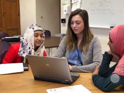 In this April 16, 2019, photo, Laken Andrews, center, a teacher at Buffalo Public School No. 37, receives training in a computer program from two student technicians, eighth grader Naureen Unaysa, left, and sixth grader Meherin Faiza, right, at the school in Buffalo, N.Y. The district and others around the country are training students to help with software and hardware issues that arise as teachers and students do more of their daily schoolwork on school-issued laptops and iPads. (AP Photo/Carolyn Thompson