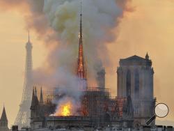  In this file photo dated Monday, April 15, 2019, with the Eiffel Tower behind, left, flames and smoke rise from the blaze at Notre Dame Cathedral in Paris that destroyed its spire and its roof but spared its twin medieval bell towers. (AP Photo/Thierry Mallet, FILE)