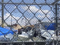 In this June 1, 2019, photo, provided by New Mexico State University professor Neal Rosendorf, migrants are seen through fencing inside a temporary outdoor encampment where they re waiting to be processed in El Paso, Texas. Rosendorf said it resembled a human dog pound. (Neal Rosendorf via AP)
