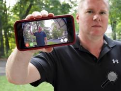 In this Tuesday, July 16, 2019, photo, Ernie Field holds up a live video of himself taken by a Ring doorbell camera at the front door at his home in Wolcott, Conn. Field won a free Ring camera and said he had to register for the app to qualify for the raffle. Now he gets alerts on his phone when a car drives by and a 30-second video when his daughter gets home from school. (AP Photo/Jessica Hill)