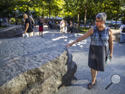 In this Thursday, Aug. 29, 2019, photo a visitor touches one of the granite slabs at the 9/11 Memorial Glade at the National September 11 Memorial & Museum in New York. When the names of nearly 3,000 Sept. 11 victims are read aloud Wednesday, Sept. 11 at the World Trade Center, a half-dozen stacks of stone will quietly salute an untold number of people who aren’t on the list. The granite slabs were installed on the memorial plaza this spring. They recognize an initially unseen toll of the 2001 terrorist att