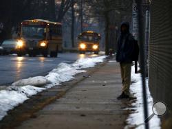 In this Feb. 5, 2019, photo, a student waits for a bus outside the abandoned John C. Clark Elementary and Middle School in Hartford, Conn. The school was closed in 2015 after toxic PCBs were found during a renovation. Many students in the neighborhood now must travel long distances to get to other schools. (AP Photo/Martha Irvine)