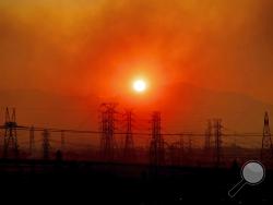 FILE - In this Friday, Oct. 11, 2019, file photo, smoke from a wildfire called the Saddle Ridge Fire hangs above power lines as the sun rises in Newhall, Calif. The destructive fire that broke out on the edge of Los Angeles began beneath a high-voltage transmission tower owned by Southern California Edison, fire officials said Monday, Oct. 14, 2019. (AP Photo/Noah Berger, File)