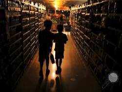 Elijah Carter 11, left, and Robert Haralson, 12, help shop for their parents in a darkened Olivers Supermarket in the Rincon Valley community, Wednesday, Oct. 23, 2019, in Santa Rosa, Calif. The west side of the store was lit by patio lights powered by a generator as power was shut off again by Pacific Gas & Electric Co. due to high fire danger. (Kent Porter/The Press Democrat via AP)
