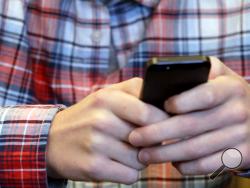 FILE - In this Oct. 24, 2013, file photo, a person checks their smartphone in Glenview, Ill. A mysterious wave of texts swept America’s phones overnight Wednesday, Nov. 6, 2019, delivering unintelligible messages that left many people mildly confused when they woke up on Thursday. (AP Photo/Nam Y. Huh, File)