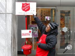 In this Friday, Nov. 15, 2019, photo, bell ringer Carolyn Harper points to two ways to donate via mobile device to the Salvation Army's annual holiday red kettle campaign on Chicago's Magnificent Mile. Cashless shoppers have a new option to give to the Army's red kettle campaign this year using their smartphone. Leaders hope adding Apple and Google payment options will boost fundraising to the campaign, which makes up 10% of The Salvation Army's annual budget. Those donations fund programs providing housing