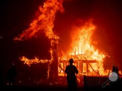 FILE - In this Nov. 8, 2018 file photo, a home burns as a wildfire called the Camp Fire rages through Paradise, Calif. Pacific Gas and Electric says it has reached a $13.5 billion settlement that will resolve all major claims related to devastating wildfires blamed on its outdated equipment and negligence. The settlement, which the utility says was reached Friday, Dec. 6, 2019, still requires court approval. (AP Photo/Noah Berger, File)