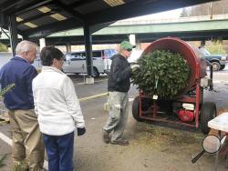 In this Wednesday, Dec. 4, 2019 photo, Bob and Jane Atkins, left, of Madison, W.Va., watch Robert Cole of French Creek Farms place their Christmas tree into a wrapping machine before being loaded onto their vehicle at the Capitol Market in Charleston, W.Va. Bob Atkins said not only are Christmas tree prices higher this year, but "there's not as many as usual, it seems to me." (AP Photo/John Raby)