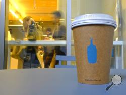 In this Thursday, Dec. 12, 2019 photo, a Blue Bottle Coffee paper to-go cup rests on a table outside one of their cafes in San Francisco. The Oakland-based chain says it's getting rid of disposable cups at two locations next year, as part of a pledge to go “zero-waste” at its 70 U.S. locations by the end of 2020. (AP Photo/Eric Risberg)