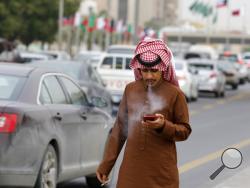 FILE - In this Monday, Dec. 9, 2019 file photo, a man smokes a cigarette as he looks at his mobile phone in Riyadh, Saudi Arabia. On Thursday, Dec. 19, 2019, the World Health Organization said worldwide, the number of men using traditional tobacco products has finally started to decline. (AP Photo/Amr Nabil)