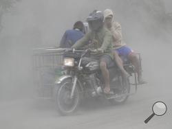 A family rides their motorcycle through clouds of ash as they evacuate to safer grounds as Taal volcano in Tagaytay, Cavite province, southern Philippines on Monday, Jan. 13, 2020. Red-hot lava is gushing from the volcano after a sudden eruption of ash and steam that forced residents to flee and shut down Manila’s airport, offices and schools. (AP Photo/Aaron Favila)