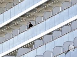 A passenger stands outside on a balcony of the cruise ship Diamond Princess anchored at the Yokohama Port Thursday, Feb. 6, 2020, in Yokohama, near Tokyo. The 3,700 people on board faced a two-week quarantine in their cabins. Health workers said 10 more people from the Diamond Princess were confirmed sickened with the virus, in addition to 10 others who tested positive on Wednesday. The 10 will be dropped off as the ship docks and transferred to nearby hospitals for further test and treatment. (AP Photo/Eu