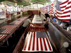 In this Saturday, Feb. 8, 2020 photo, workers print U.S. flags using a silkscreen, at the Diba Parcham Khomein factory in Heshmatieh village, a suburb of Khomein city, in central Iran. Workers at a small Iranian factory diligently add all 50 stars and 13 bars to American flags while carefully imprinting the Star of David on those of Israel. That's even as all their work is destined to go up in smoke. This factory serves as a major producer for the American and Israeli flags constantly burned at demonstratio
