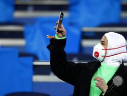A fan wearing a protective mask takes a picture with her cell phone prior the Champions League, round of 16, first leg soccer match between Real Madrid and Manchester City at the Santiago Bernabeu stadium in Madrid, Spain, Wednesday, Feb. 26, 2020. (AP Photo/Manu Fernandez)