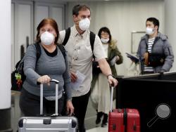 Travelers wear protective mask as they walk through in terminal 5 at O'Hare International Airport in Chicago, Sunday, March 1, 2020. (AP Photo/Nam Y. Huh)