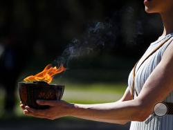 FILE - In this March 12, 2020, file photo, an actress, playing the role of the priestess, holds the flame during the flame lighting ceremony at the closed Ancient Olympia site, birthplace of the ancient Olympics in southern Greece. The Olympic flame from Greece is set to arrive in Japan even as the opening of the the Tokyo Games in four months is in doubt with more voices suggesting the games should to be postponed or canceled because of the worldwide virus pandemic. (AP Photo/Thanassis Stavrakis, File)