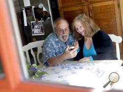 Seen through their kitchen window, Allan and Debbie Cameron contact their grandchildren via the internet Wednesday, March 25, 2020, in Chandler, Ariz. Debbie, 68, has asthma which makes her one of the people most at risk from the new coronavirus. The Cameron's now she see their children and grandchildren from the other side of a window or a phone. (AP Photo/Matt York)